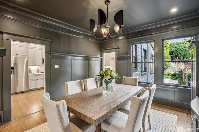 dining space featuring a chandelier, a decorative wall, light wood-type flooring, and crown molding