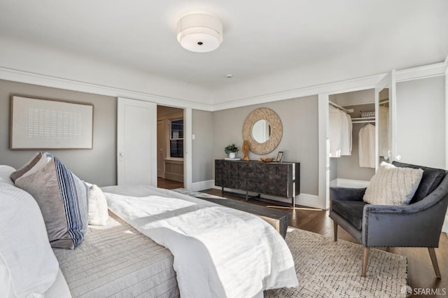 bedroom with a closet, a spacious closet, baseboards, and wood finished floors