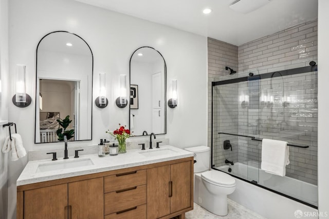 bathroom with double vanity, shower / bath combination with glass door, a sink, and toilet