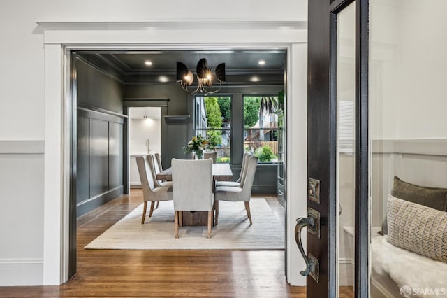 dining room featuring ornamental molding, a decorative wall, a notable chandelier, and wood finished floors