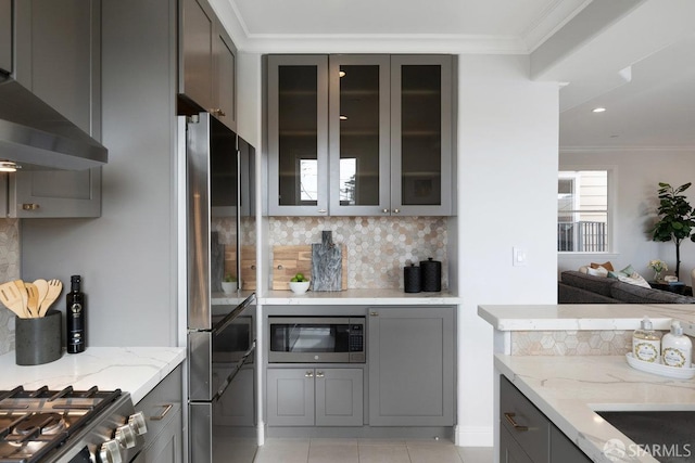 kitchen featuring gray cabinetry, stainless steel appliances, decorative backsplash, light stone counters, and ornamental molding