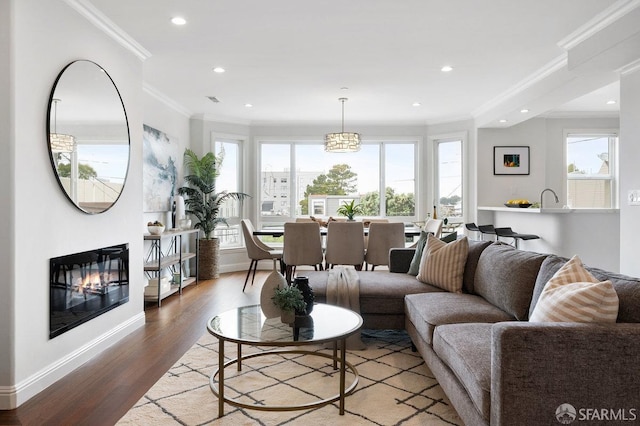 living room with ornamental molding, plenty of natural light, wood finished floors, recessed lighting, and a glass covered fireplace