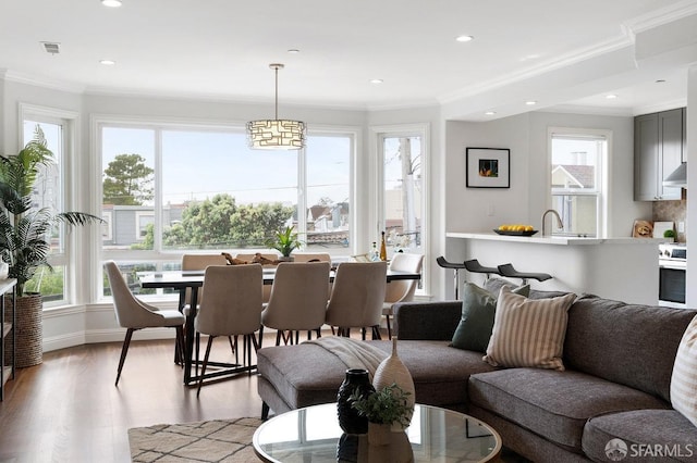 living room featuring plenty of natural light, light wood-style floors, crown molding, and recessed lighting