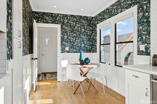 dining space with ornamental molding, wainscoting, light wood finished floors, and wallpapered walls