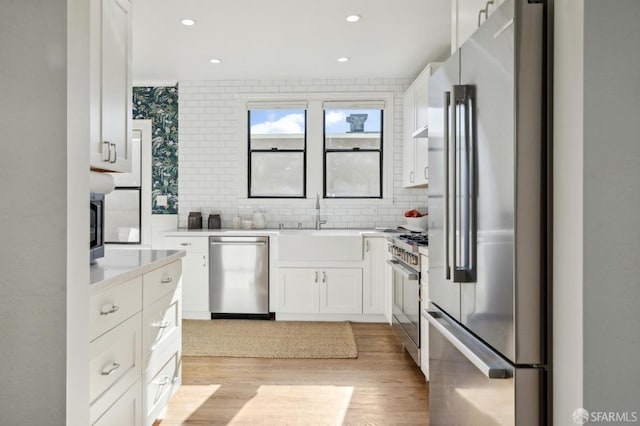 kitchen featuring white cabinets, high end appliances, light countertops, light wood-style floors, and backsplash