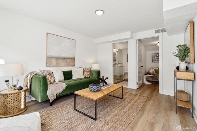 living room with light wood-type flooring, visible vents, and baseboards