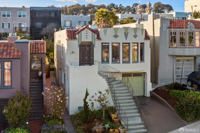 view of front of house featuring a tile roof, stucco siding, an attached garage, and stairs