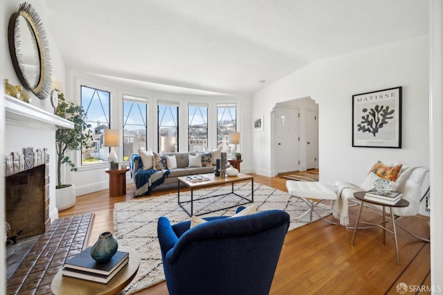 living room with lofted ceiling, a brick fireplace, wood finished floors, and baseboards