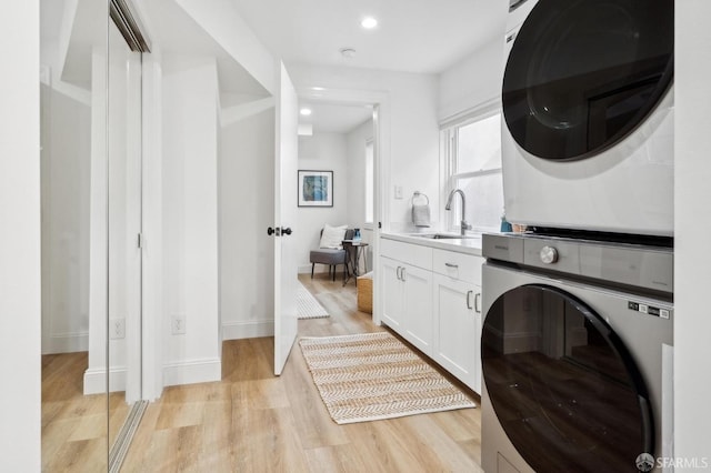 laundry area featuring cabinet space, light wood-style floors, stacked washing maching and dryer, a sink, and recessed lighting