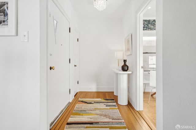 hall with an inviting chandelier, wood finished floors, and baseboards