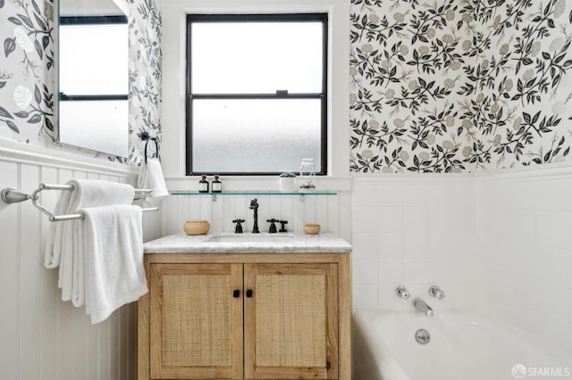 full bathroom featuring wainscoting, vanity, a bathing tub, and wallpapered walls