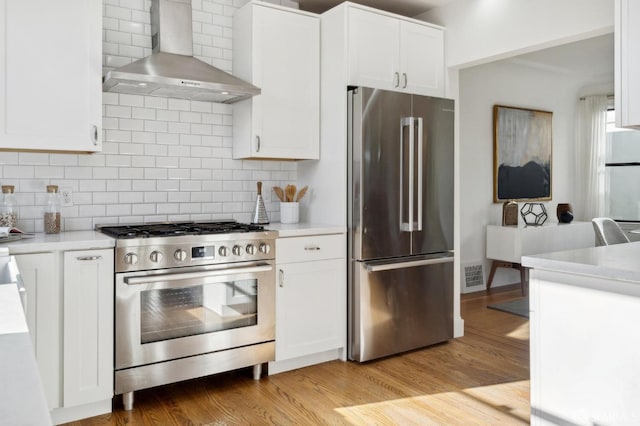 kitchen featuring appliances with stainless steel finishes, light wood-type flooring, decorative backsplash, and wall chimney exhaust hood