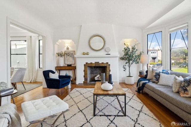 living room with vaulted ceiling, a fireplace, wood finished floors, and baseboards