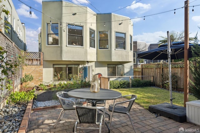 rear view of house with a patio, outdoor dining space, a fenced backyard, and stucco siding