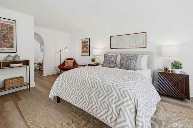 bedroom featuring arched walkways, baseboards, and wood finished floors