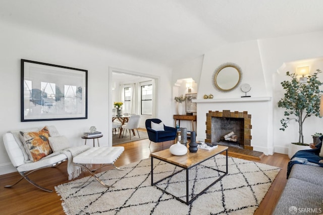 living room featuring a tile fireplace, vaulted ceiling, baseboards, and wood finished floors