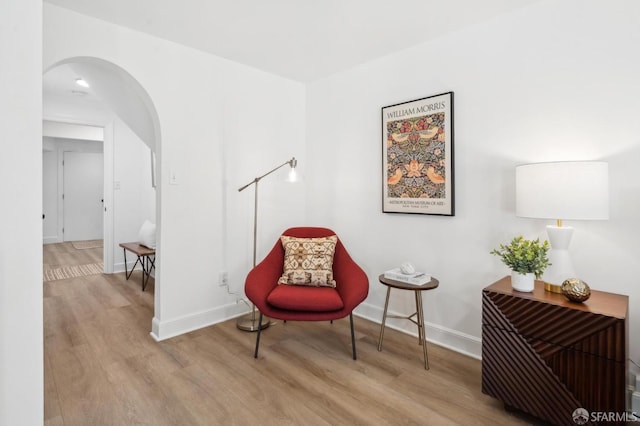 living area featuring baseboards, arched walkways, and wood finished floors