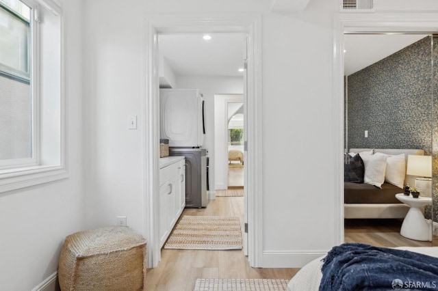 hall with stacked washer and dryer, baseboards, and light wood-style floors