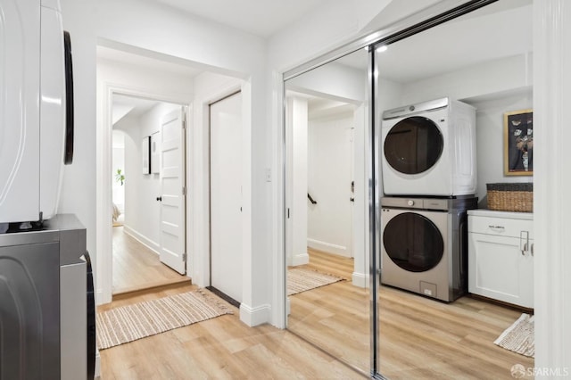 laundry room featuring baseboards, light wood-style floors, cabinet space, and stacked washer / drying machine