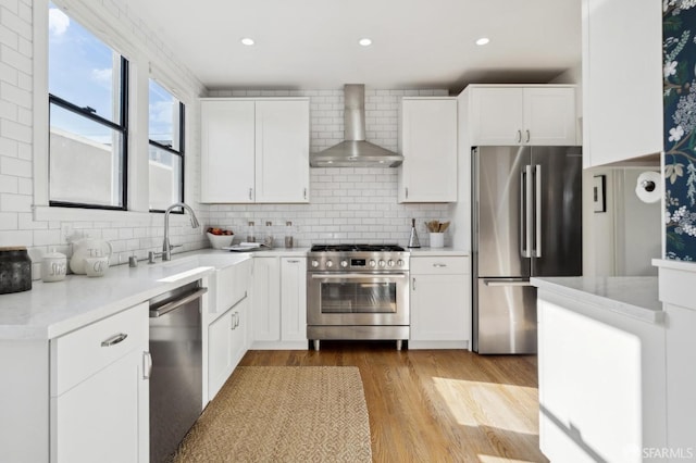 kitchen with decorative backsplash, wall chimney exhaust hood, appliances with stainless steel finishes, wood finished floors, and a sink