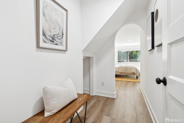 hallway with light wood-type flooring, baseboards, and arched walkways