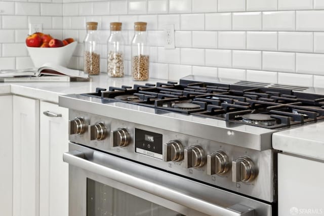 room details with gas range, white cabinetry, decorative backsplash, and light countertops