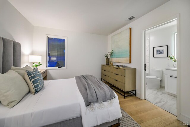 bedroom with wood finished floors, visible vents, and ensuite bath