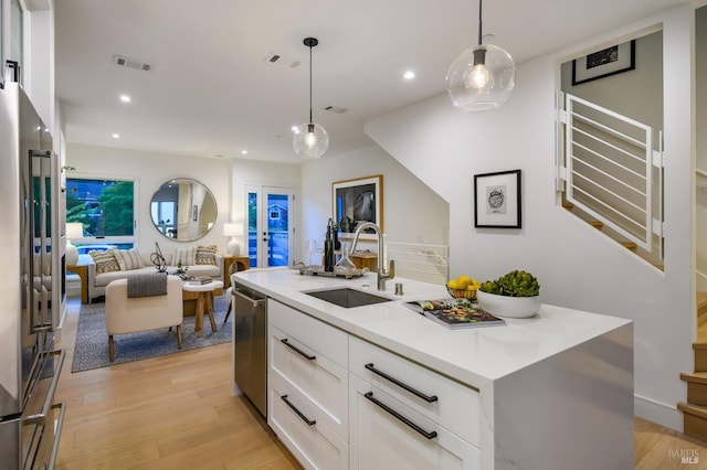 kitchen with white cabinetry, a sink, light wood-style floors, stainless steel appliances, and visible vents