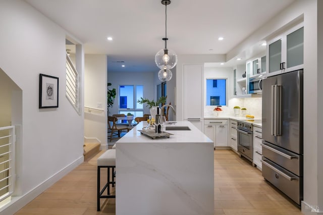 kitchen with tasteful backsplash, a kitchen island with sink, light wood-style floors, a sink, and premium appliances