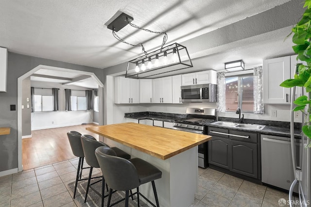 kitchen featuring white cabinetry, a sink, appliances with stainless steel finishes, a breakfast bar, and butcher block counters