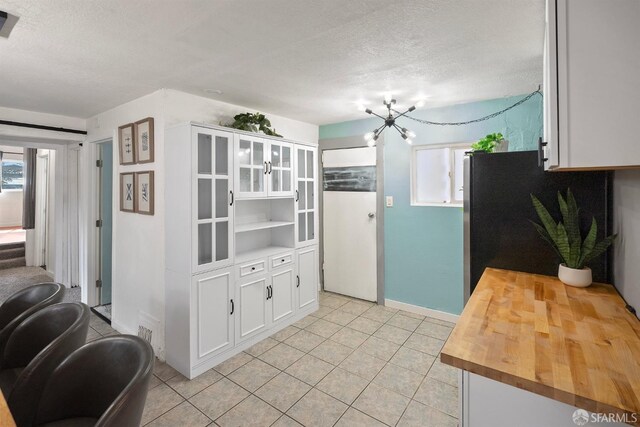 kitchen with light tile patterned floors, a textured ceiling, white cabinets, a chandelier, and butcher block counters