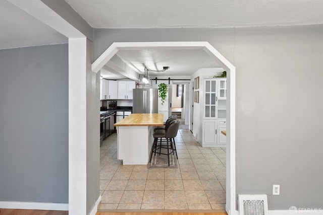 kitchen featuring a kitchen breakfast bar, visible vents, white cabinetry, wooden counters, and freestanding refrigerator