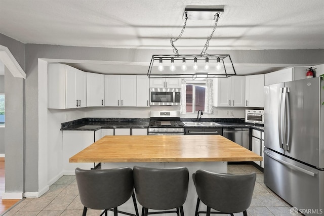 kitchen with light tile patterned floors, white cabinets, a sink, stainless steel appliances, and a kitchen bar