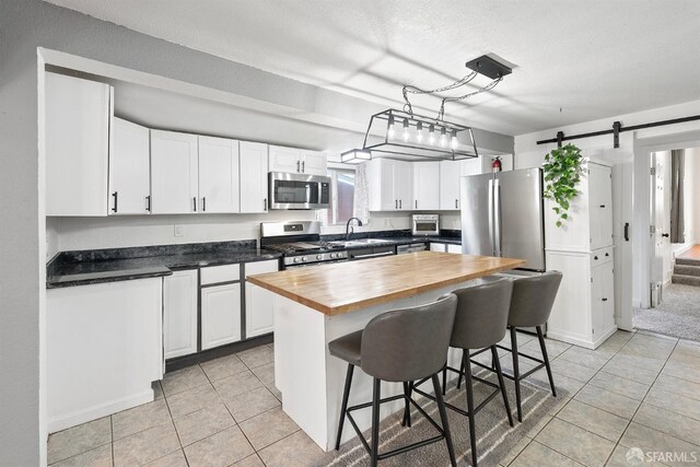 kitchen with wood counters, light tile patterned floors, a sink, appliances with stainless steel finishes, and a barn door