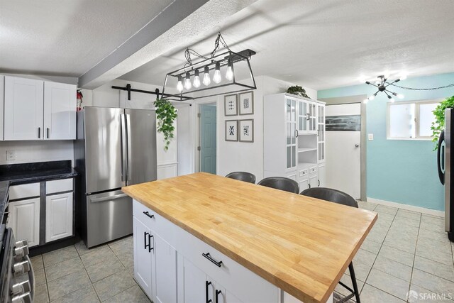kitchen with a textured ceiling, white cabinets, appliances with stainless steel finishes, a barn door, and light tile patterned flooring