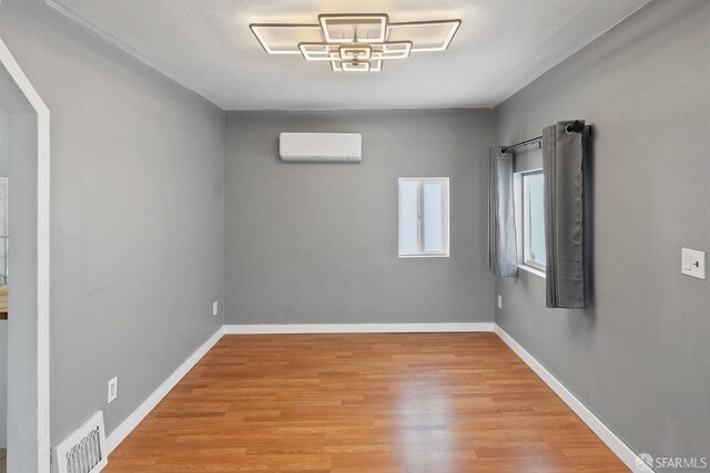 spare room with wood finished floors, visible vents, a wall mounted air conditioner, and baseboards