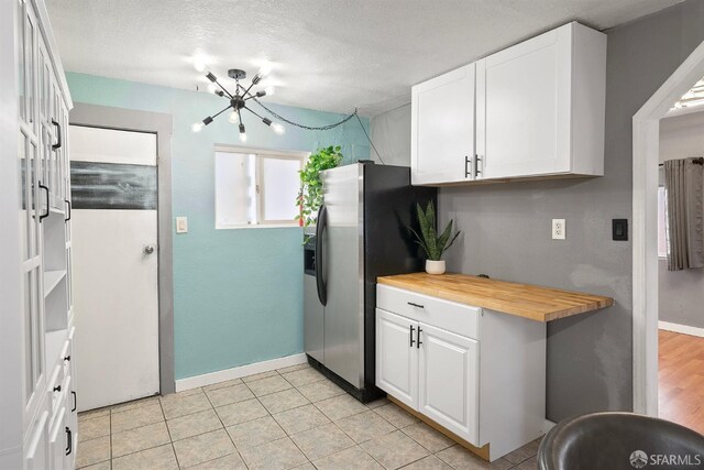 kitchen with butcher block countertops, a notable chandelier, white cabinetry, baseboards, and stainless steel fridge with ice dispenser