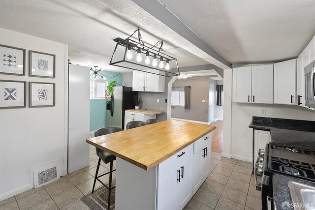 kitchen featuring light tile patterned floors, wood counters, stainless steel appliances, white cabinets, and visible vents