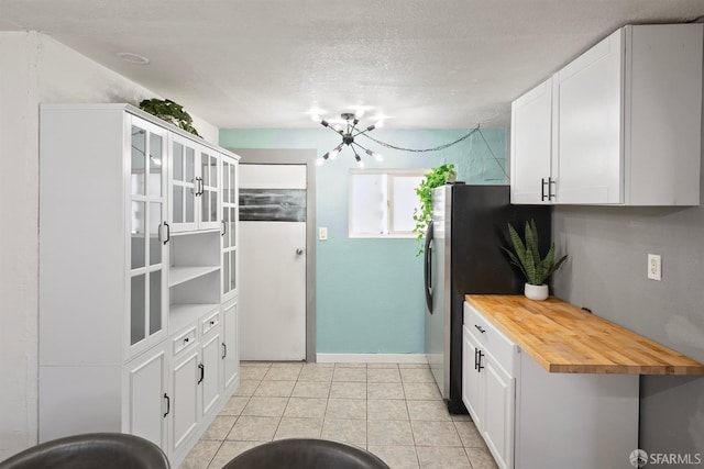 kitchen featuring butcher block countertops, light tile patterned floors, a notable chandelier, baseboards, and white cabinets