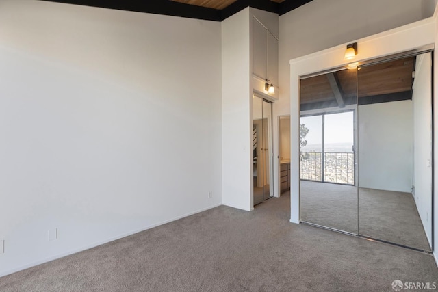 unfurnished bedroom with a high ceiling, beamed ceiling, and carpet