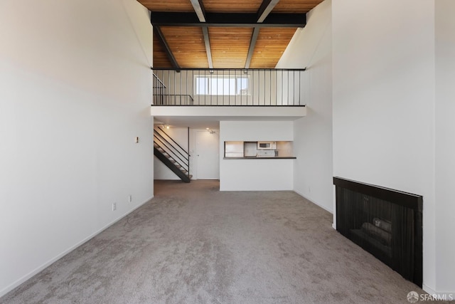 unfurnished living room featuring wooden ceiling, a fireplace, carpet flooring, a towering ceiling, and stairs