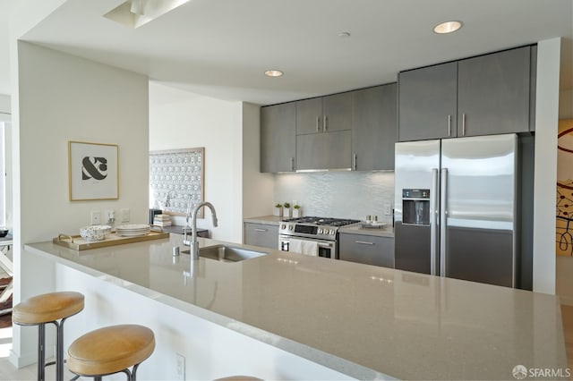 kitchen featuring sink, backsplash, kitchen peninsula, high quality appliances, and a breakfast bar