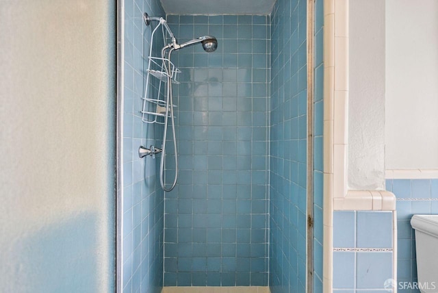 bathroom with toilet, a tile shower, and tile walls