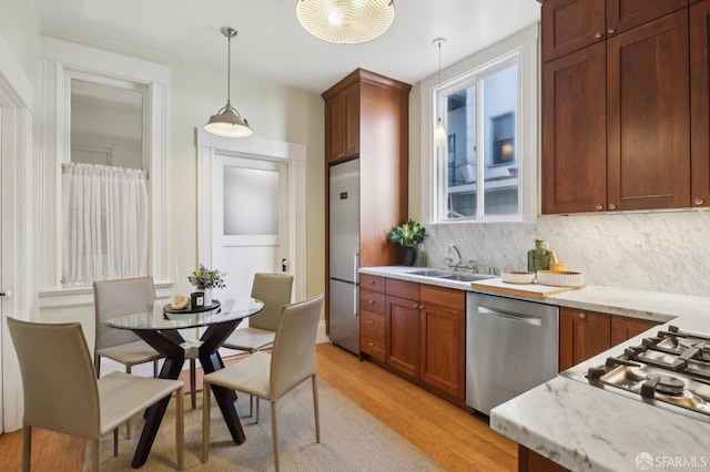 kitchen with light wood finished floors, decorative backsplash, appliances with stainless steel finishes, pendant lighting, and a sink