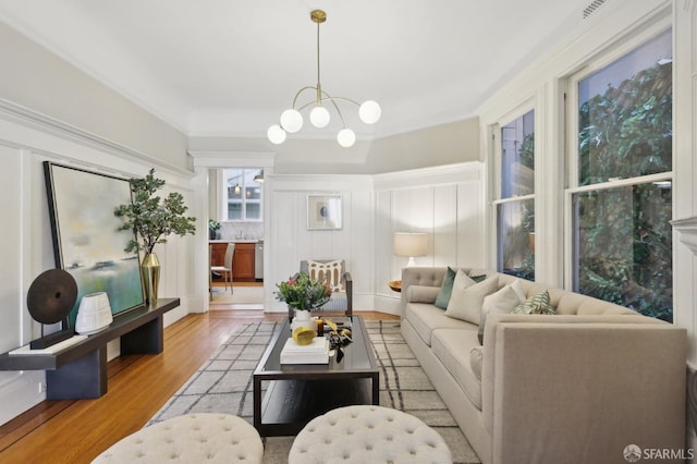 living area with an inviting chandelier, light wood-style flooring, visible vents, and a decorative wall