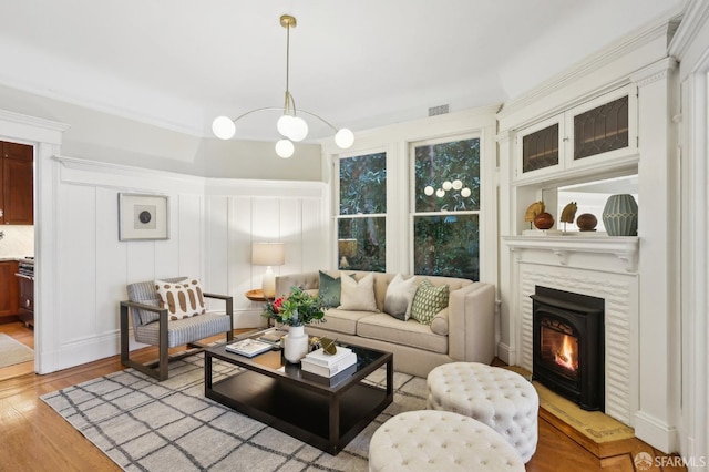 living area featuring light wood-style floors, a warm lit fireplace, visible vents, and a decorative wall