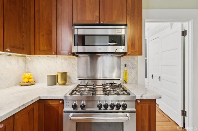 kitchen with stainless steel appliances, tasteful backsplash, brown cabinetry, and light stone countertops