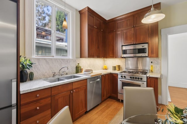 kitchen featuring a sink, hanging light fixtures, appliances with stainless steel finishes, light stone countertops, and tasteful backsplash