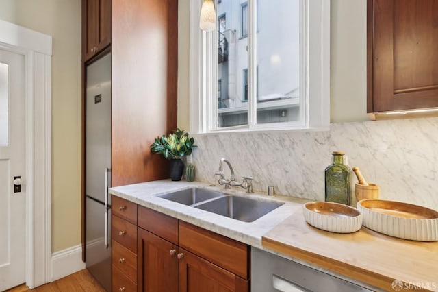 kitchen with light stone countertops, stainless steel built in fridge, a sink, decorative backsplash, and brown cabinets