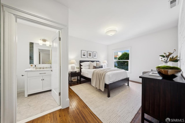 bedroom with baseboards, ensuite bath, visible vents, and wood finished floors